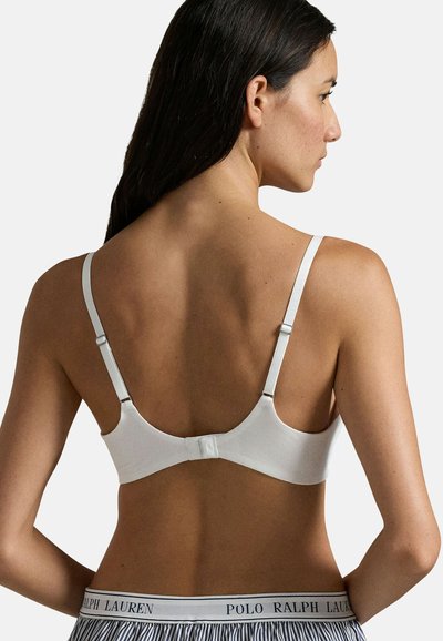 Bra bianco senza cuciture con spalline regolabili, texture liscia e chiusura con gancio e asola sul retro. Presenta un dettaglio del logo sulle spalline.