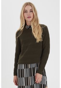 Olivgrüner Rundhals-Pullover mit strukturierten horizontalen Streifen, kombiniert mit einem schwarz-weißen gestreiften Rock mit unterschiedlichen Breiten.