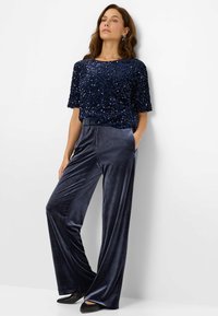 Haut bleu marine à manches courtes orné de sequins avec un col rond, associé à un pantalon large en velours doux assorti. Des chaussures noires complètent la tenue.