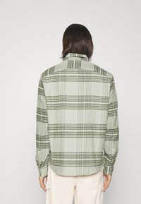 Camisa de cuadros verde y negro, de botones, con mangas largas, hecha de un tejido ligero, que presenta un dobladillo curvado y mangas con puños.