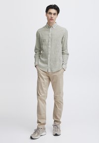 Camisa de botones a rayas verde y blanca combinada con pantalones beiges y zapatillas grises. La camisa cuenta con cuello y mangas largas.