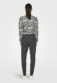 Långärmad skjorta med ett svart och vitt zebramönster, tillsammans med mörkgrå snäva byxor och ljusa skor.