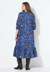 Abito blu con stampa leopardata, maniche a 3/4, orlo arricciato e tessuto leggero. Completato con stivali al ginocchio in pelle marrone.