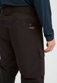 Schwarze Outdoor-Hosen mit einer Reißverschlusstasche und einer seitlichen Cargo-Tasche. Mit einem orangefarbenen "NORTH BEND"-Logo auf der Rückseite. Flexibles, glattes Material.