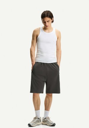 Biely bezrukávový top, tmavošedé športové šortky s vreckami, biele ponožky a svetlošedé bežecké topánky. Jednoduchý, neformálny outfit.