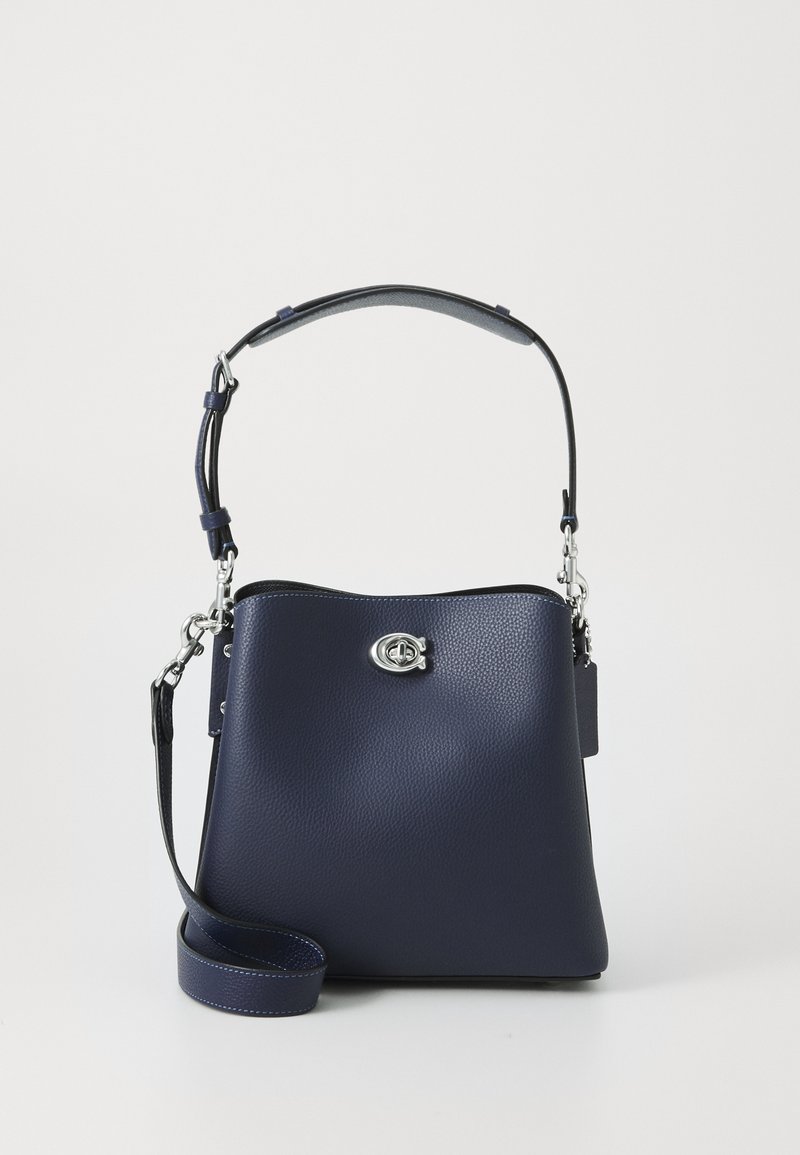 Sac à main en cuir bleu marine avec fermoir argenté, poignée supérieure ajustable et bandoulière amovible sur fond blanc uni.