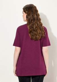 Camiseta de manga corta, de color púrpura, hecha de una tela suave. Corte relajado con un dobladillo recto. Diseño minimalista, sin patrones ni detalles visibles.