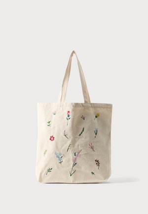Sac cabas beige avec deux poignées, décoré de petites fleurs brodées colorées éparpillées sur le devant.