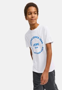 Camiseta blanca de algodón con un gráfico circular azul que dice "JACK & JONES 1990 COLLECTORS CREW" y el logo. Pantalones cortos grises con costuras visibles.