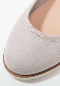 Lys rosa stof flad sko med en glat tekstur, rund tå og en blød elastisk krave. Har en tan, let forhøjet sål med hvid trim.