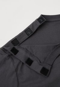 Σκοτεινό γκρι ρούχο με τρεις μαύρες θηλιές για εύκολο φόρεμα και ρύθμιση, ξεκουμπωμένο.