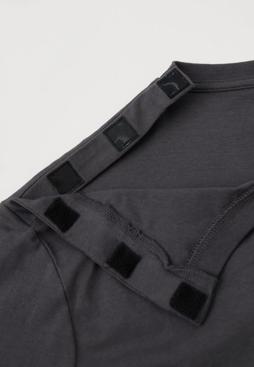 Prenda de color gris oscuro en el hombro con tres cierres de gancho y bucle negros, desabrochada para facilitar su uso y ajuste.