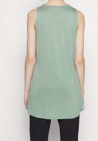 Tunika verde senza maniche realizzata in tessuto leggero, con scollatura tonda e un orlo posteriore leggermente più lungo per una vestibilità rilassata.