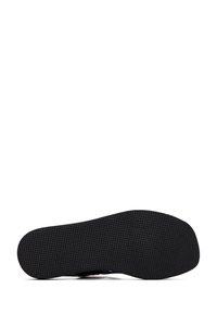 Black shoe featuring a textured rubber sole, flat design, and minimal accents. The sole is smooth with a patterned grip for traction.