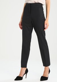 Sorte skræddersyede bukser med slim fit, høj talje og rene linjer. Stoffet har en glat struktur med en subtil glans. Bæres med sorte hæle.