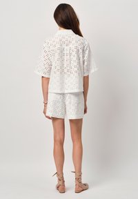 Witte katoenen set bestaande uit een top en shorts met opengewerkte patronen. De top heeft korte mouwen en een kraag, terwijl de shorts tot halverwege de dij komen.