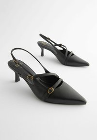 Mustat nahkaiset slingback-korkokengät, joissa on terävät varpaat, ristiin risteilevät hihnat ja kultasävyiset yksityiskohdat, asennettuna kohtuulliselle korkokengälle.