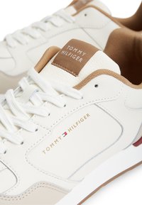 Λευκό και μπεζ αθλητικό παπούτσι Tommy Hilfiger με κορδόνια, επενδυμένο γιακά και λογότυπο της μάρκας στο πλάι και στη γλώσσα.