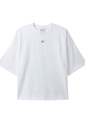 Camiseta blanca de manga corta con cuello redondo y un pequeño parche con el logo "ck" en rojo y negro, centrado debajo del cuello.