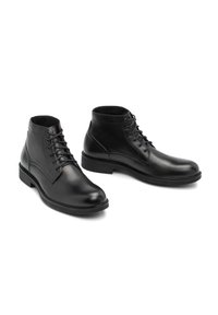 Botas de cuero negras hasta el tobillo con un acabado suave, puntera redonda y diseño de cordones. Cuentan con un tacón bajo y detalles texturizados a lo largo de los costados.
