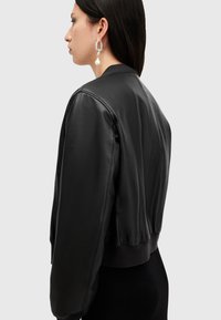 Chaqueta bomber de cuero negro con un diseño cropped, dobladillo acanalado y costuras de acento. Presenta una textura suave y mangas anchas y relajadas.