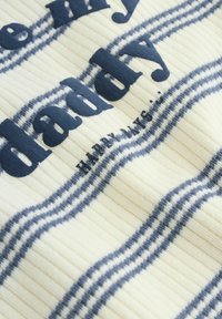 Tkanina z navpičnimi črto v kremni in mornarsko modri barvi, na kateri je poudarjeno besedilo 'daddy'. Material ima rebrasto teksturo s kontrastnimi horizontalnimi črtami.