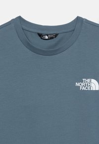 Σκούρο μπλε μπλουζάκι με στρογγυλή λαιμόκοψη, με το λογότυπο "The North Face" σε λευκό στο μπροστινό αριστερό μέρος του στήθους και μια μαύρη ετικέτα μεγέθους μέσα στον γιακά.