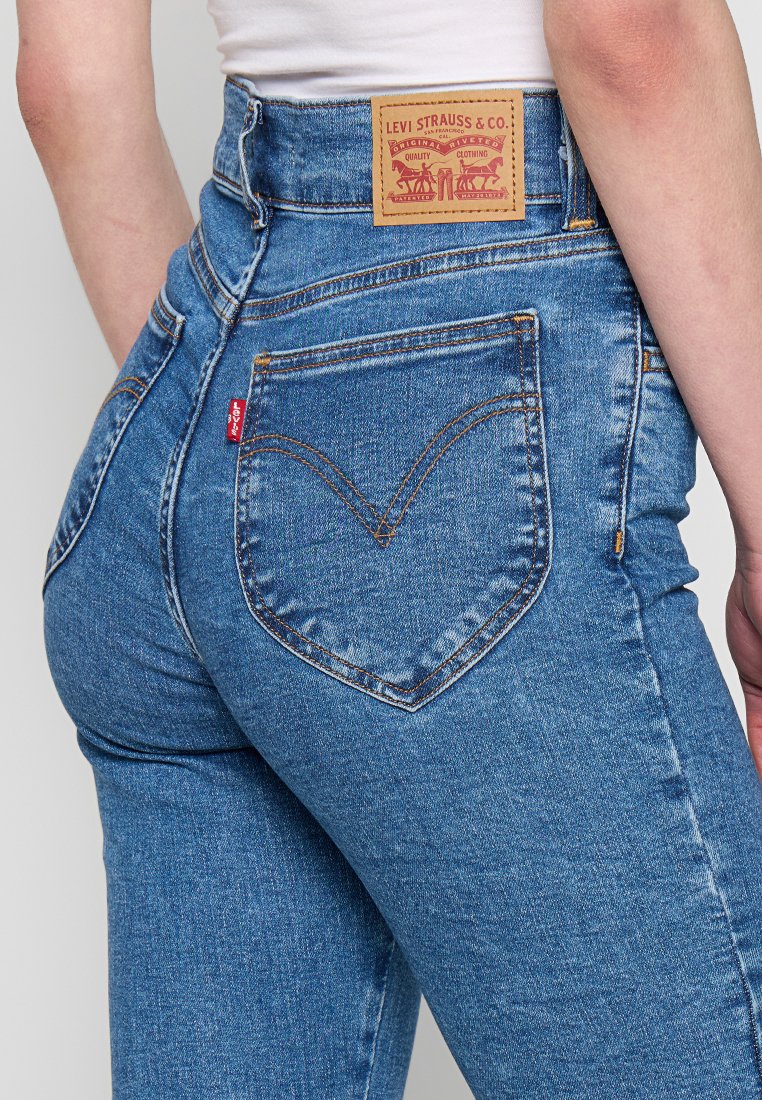 Acercamiento al bolsillo trasero de unos jeans Levi's azules, con el icónico bordado en forma de arcuado, la etiqueta roja de Levi's y la etiqueta de cuero de Levi Strauss & Co. en la cinturilla.