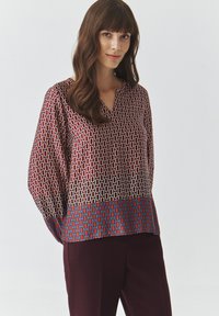 Langsleeve blouse in bordeaux met geometrisch patroon; met een v-hals en een blauwe zoom, zijdezachte textuur en een relaxte pasvorm.
