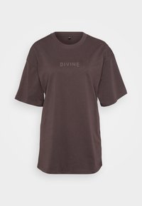 Hnědé tričko s krátkým rukávem vyrobené z bavlny, s kulatým výstřihem a nápisem "DIVINE" vytištěným v mírně tmavší barvě přes hruď.