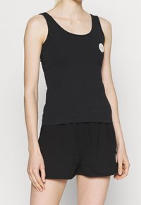 Débardeur noir en coton doux, doté d'un col arrondi et d'une coupe ajustée. Comprend un petit écusson logo à l'avant.