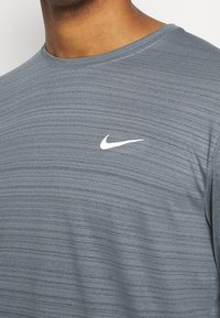 Graues Sport-T-Shirt mit Rundhalsausschnitt, aus strukturiertem Stoff. Hat ein kleines weißes Nike-Logo auf der Brust.