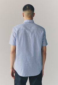 Kortærmet skjorte med button-down krave, med lodrette blå og hvide striber, glat stof og en buet kant bagpå.