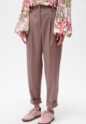 Pantalons marron ajustés avec une taille haute, dotés de deux boutons avant et de bas de pantalons à revers, associés à des baskets rose clair.