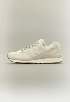 Baskets New Balance beige clair avec une texture en daim, des lacets et une semelle coussinée, vues de côté sur un fond neutre.