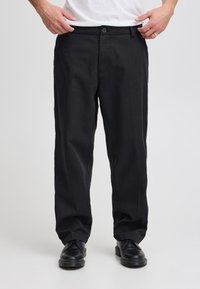 Svarte bukser med rett passform, laget av teksturert stoff. Har knappelukking og subtile frontlommer. Kombinert med svarte sko.