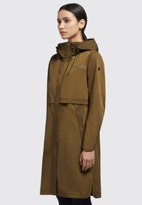 Parka impermeabile marrone con cappuccio, due tasche laterali, cordini regolabili e un semplice logo sul petto. Texture liscia e opaca.