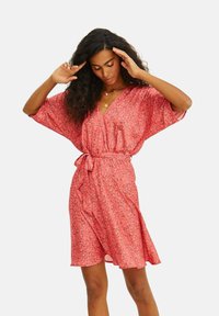 Šaty s květinovým vzorem v korálové barvě, s výstřihem do V, volnými rukávy a páskem v oblasti pasu. Měkká tkanina s volním střihem.