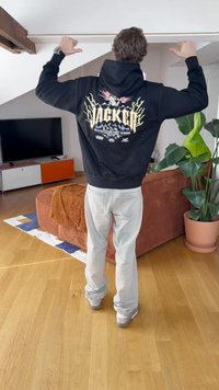 Felpa nera con cappuccio e una grafica colorata sulla schiena, che presenta un leone e montagne. Indossata con jeans grigi chiari e sneakers argento.