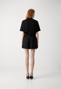 Black short-sleeve top paired with black shorts. The outfit features a loose fit, textured fabric, and is complemented by black heeled sandals.