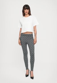 White cropped t-shirt with short sleeves, paired with black leggings featuring a repeating gray geometric pattern and black high heels.
