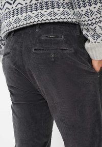 Pantaloni in corduroy neri con righe verticali, dotati di due tasche posteriori e chiusura con un solo bottone. Tessuto texturizzato visibile.