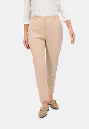 Pantalons beige ajustés avec poches latérales, coupe droite et fermeture par bouton. Tissu doux avec une texture minimale, associés à des mocassins à enfiler.