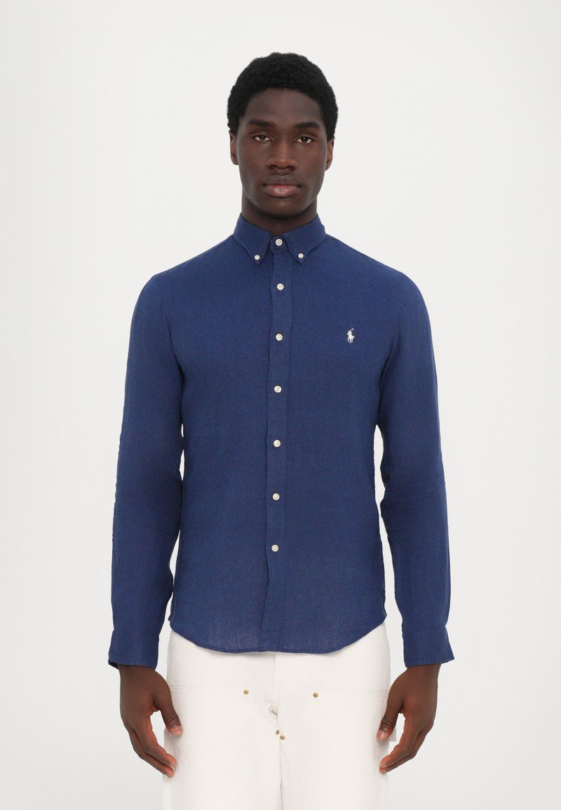 Temno moder srajca z gumbki, z ovratnikom, dolgimi rokavi in majhnim logotipom na prsih; izdelana iz teksturiranega materiala.