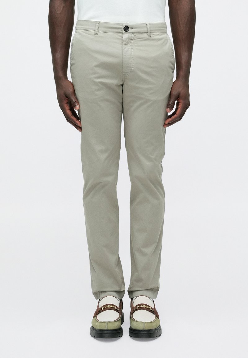 Ανοιχτό γκρι chinos slim-fit με ομαλή υφή  και εμπρόσθιες τσέπες, σε συνδυασμό με πολύχρωμα αθλητικά παπούτσια που διαθέτουν διακοσμητική αλυσίδα.