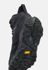 Scarpa sportiva nera con tomaia in mesh testurizzato, lati rinforzati e suola in gomma robusta con un motivo di tassellatura distintivo.