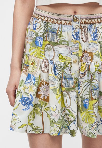 Φούστα με τροπικό σχέδιο που περιλαμβάνει φοίνικες, λουλούδια, χελώνες, κοχύλια και μοτίβα γραμματοσήμων σε πράσινους, μπλε, κίτρινους και καφέ τόνους.