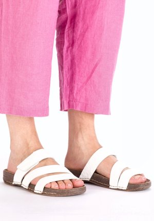 Sandales à glissière en cuir blanc avec trois larges lanières, dotées d'une semelle texturée marron. Portées avec un pantalon cropped rose et ample.