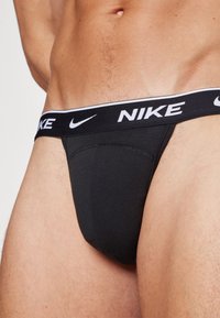 Schwarze Nike-Tanga aus weichem Material, mit einem breiten elastischen Bund und weißem Branding. Das Design ist minimalistisch und körperbetont.