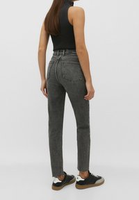 Jeans de tiro alto y pierna recta en mezclilla negra desgastada con dobladillo deshilachado, combinados con una blusa sin mangas de canalé negra y zapatillas negras.
